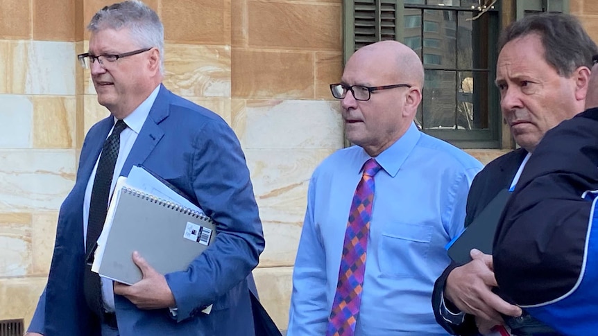 Magistrate Bob Harrap walking with two men walking beside him