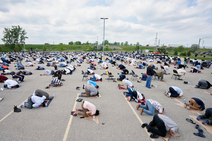 Hundreds of Muslims pray in an empty car park where a funeral is being held. 
