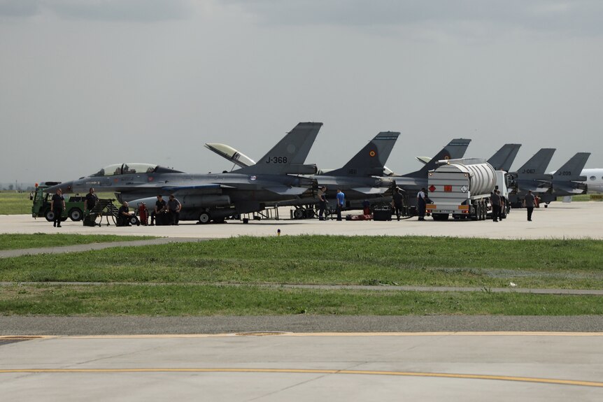 Six grey-coloured combat aircraft lined up at a hangar