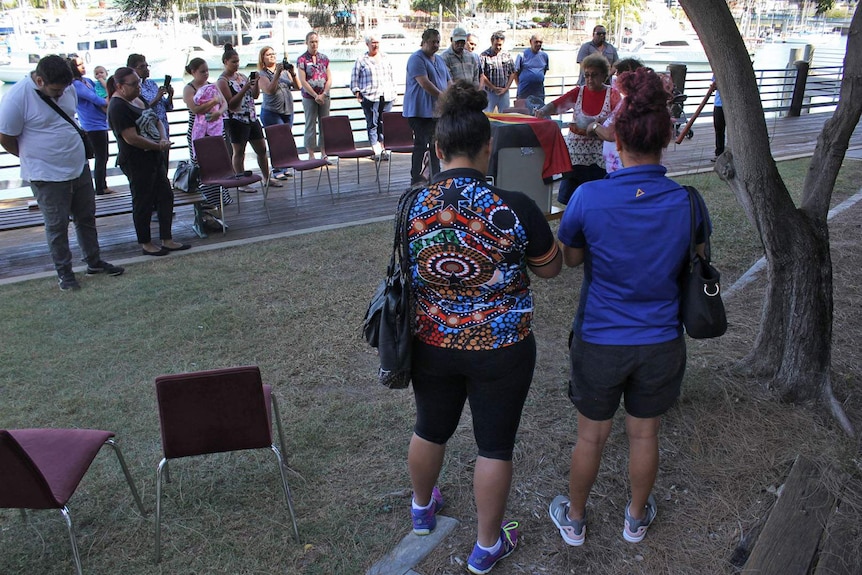 Aboriginal smoking ceremony - people stand around a box with the Aboriginal flag draped over it.