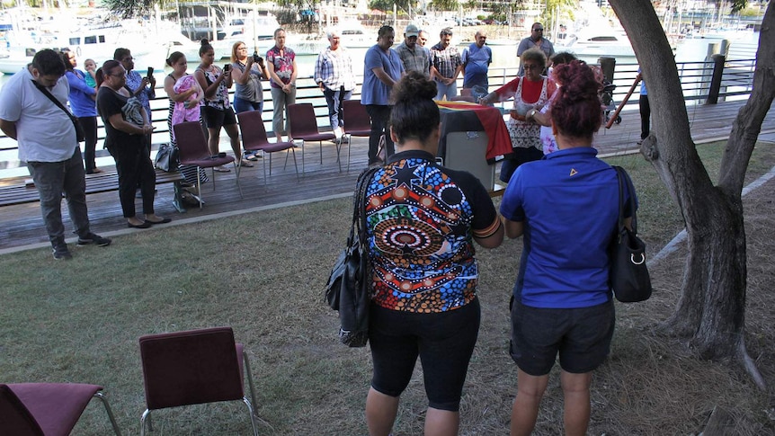 Aboriginal smoking ceremony - people stand around a box with the Aboriginal flag draped over it.