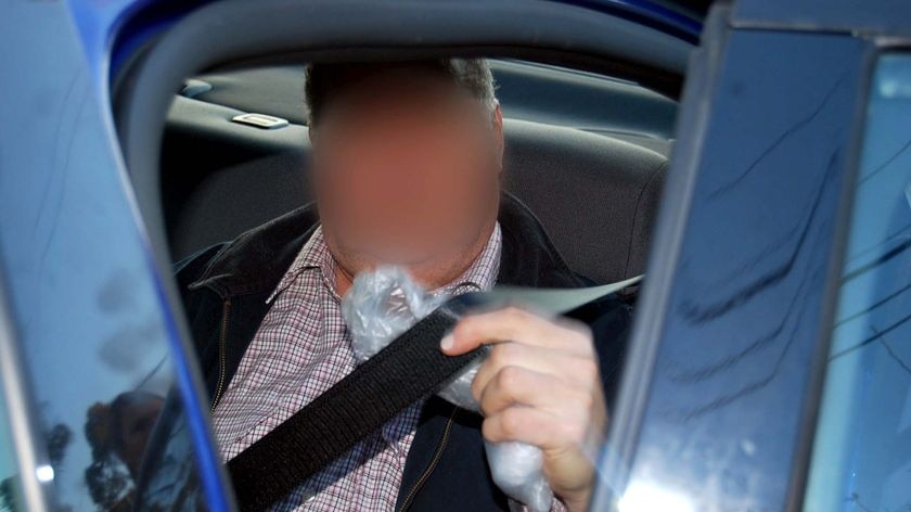 A former NSW doctor sits in the back of a police car