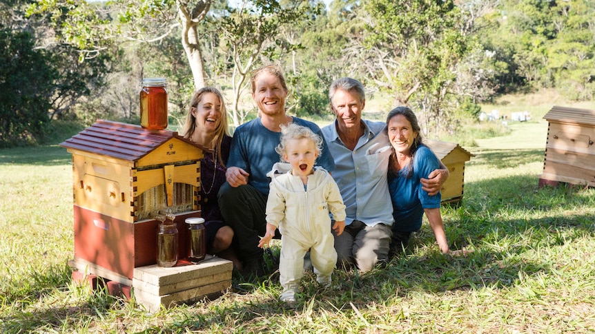 Five members of the Anderson family sitting in the grass with a Flow Hive and smiling.