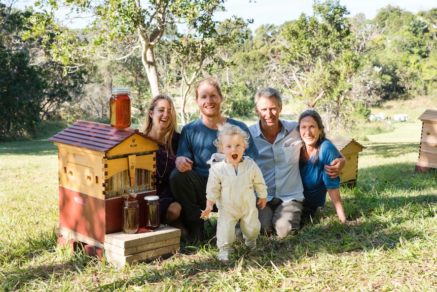 Five members of the Anderson family sitting in the grass with a Flow Hive and smiling.
