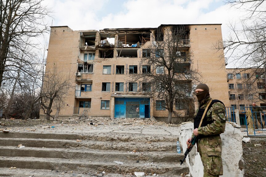 Soldier stands outside of building damaged by drone strike.