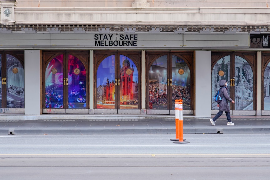 A woman walks past a "Stay Safe Melbourne" sign on a mostly-empty city street