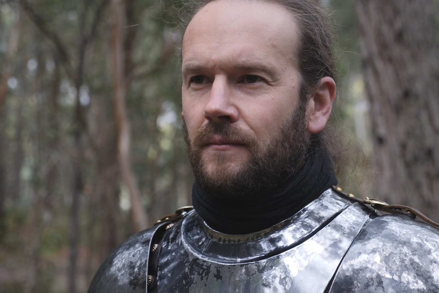 A man wearing metal armour stands in the bush