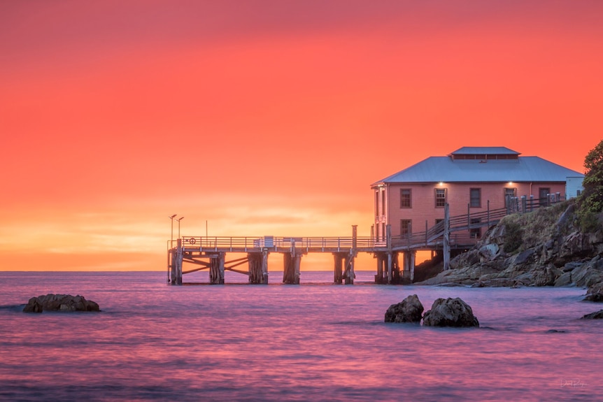 Tathra wharf pictured at sunset in story about encouraging tourists to visit regional Australia after natural disasters.