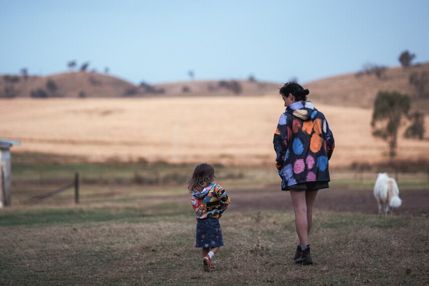 Lisa and a young child wearing colourful coats walk through a paddock