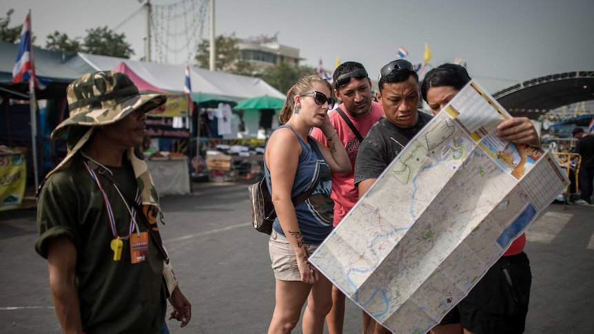 An anti-government demonstrator looks at tourists checking a map as they reached a protest site in Bangkok