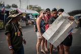 An anti-government demonstrator looks at tourists checking a map as they reached a protest site in Bangkok