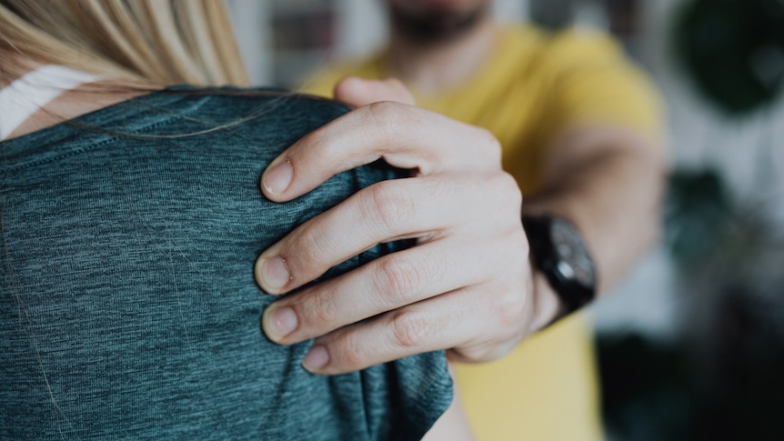 A man in a yellow shirt grabs a woman's shoulder