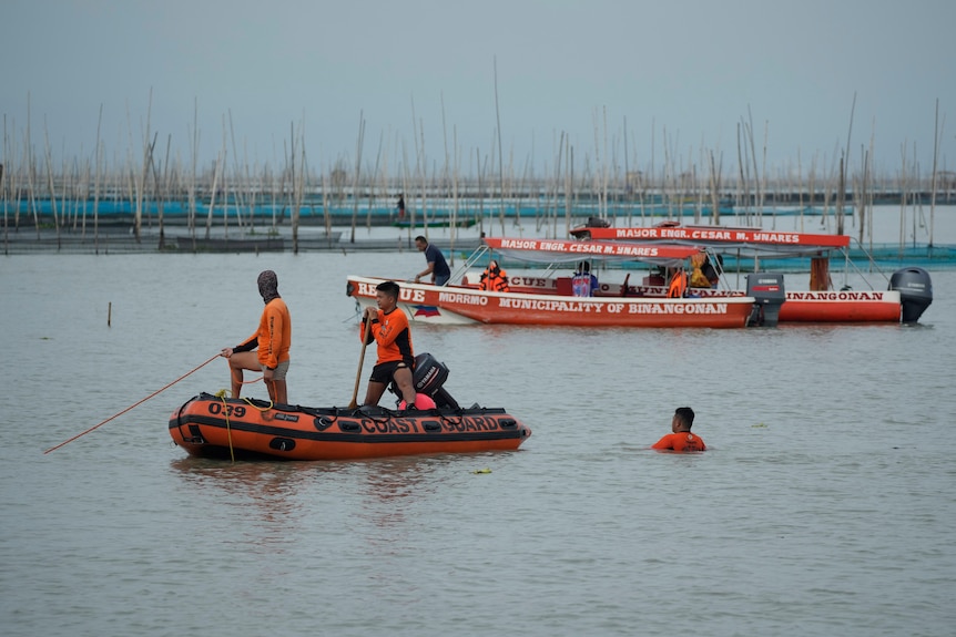 Men in dinghy put ropes into the water. A man in bright orange is in the water up to his shoulders.