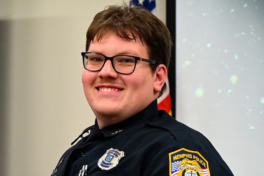 A man smiles wearing a police uniform and glasses. 