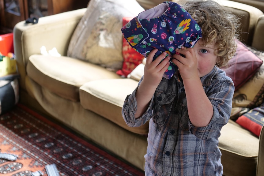 Three year old boy holds space-patterned cloth nappy in front of his face