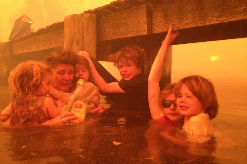 A woman and children sheltering from a fire under a jetty