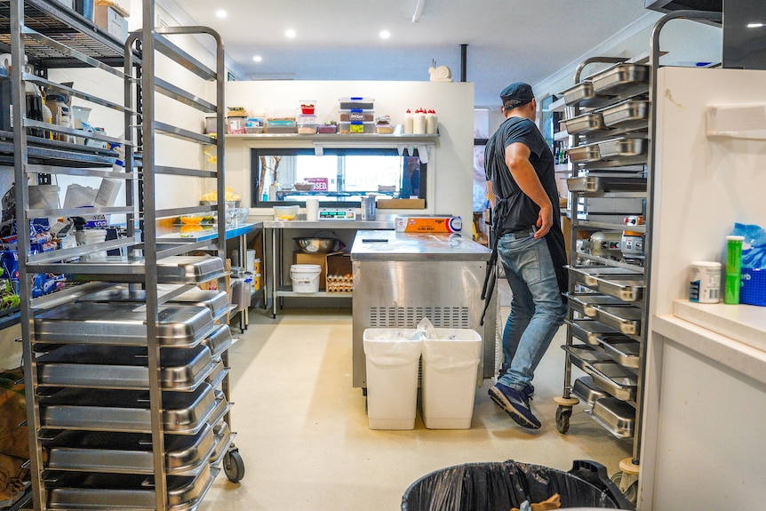 A man stands in a commerical kitchen with racks of scrolls ready for the oven