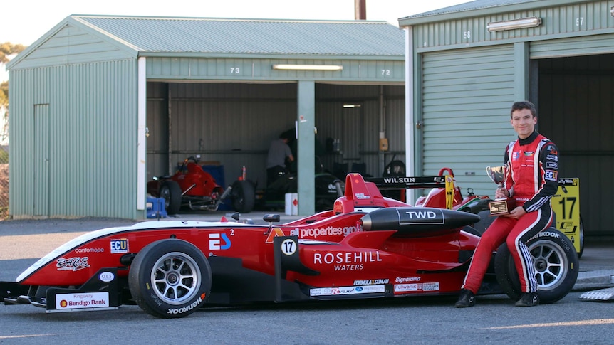 Calan Williams sitting on the back of a red racing car.
