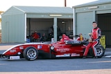 Calan Williams sitting on the back of a red racing car.