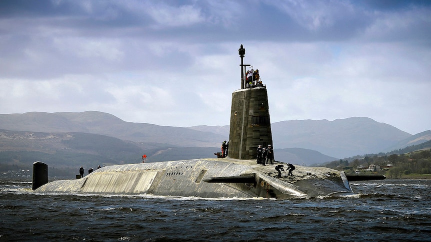 Sailors stand on board the partly-submerged submarine HMS Vigilant.