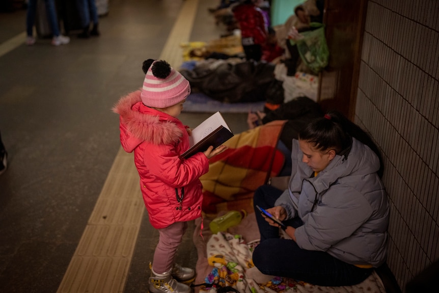 A girl looks at a notebook next to her mother as they shelter in the Kyiv subway.