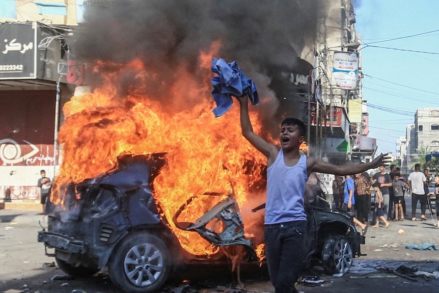 A boy next to a burning vehicle.
