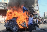 A boy next to a burning vehicle.