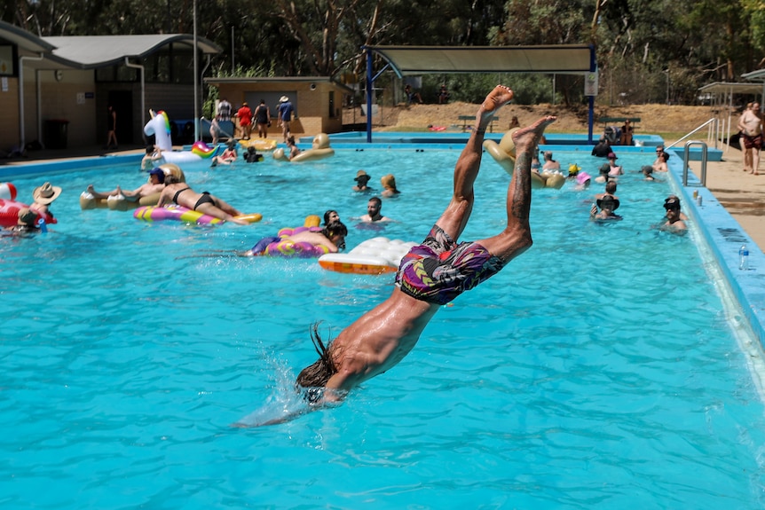 Man dives in to bright blue country swimming pool with other people lounging nearby