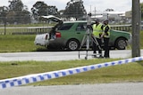 two police officers in hi-vis standing with a piece of equipment on a road with police tape in the foreground