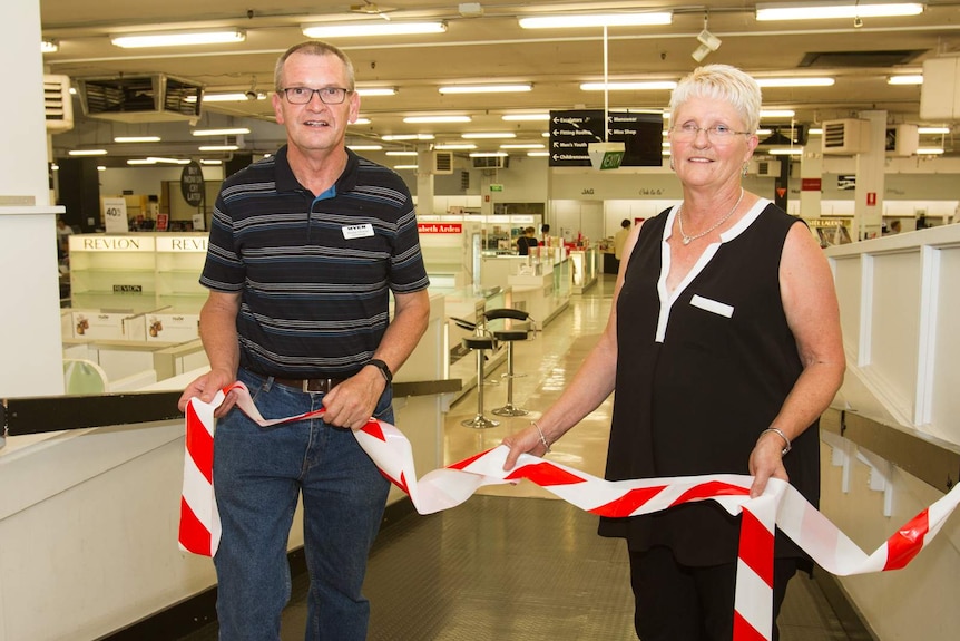 A man with a Myer badge and a woman holding closed off red and white tape standing in an almost empty department store