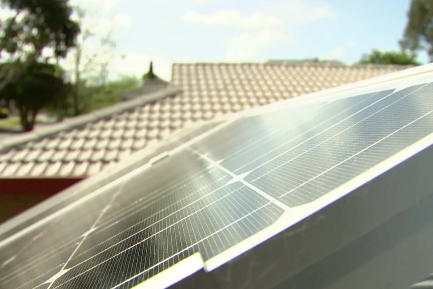 A solar panel in the foreground with a tiled roof in the background.