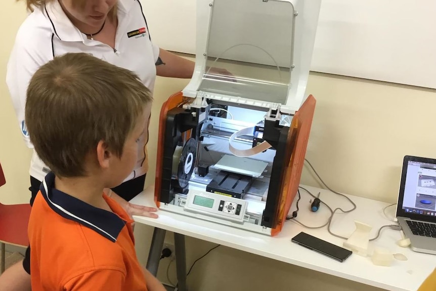 A picture of a teacher and boy looking at a 3D printer in Broome.