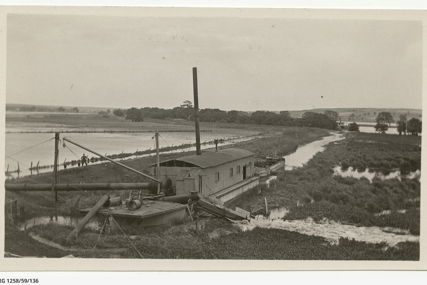 A black and white photo of an old barge with pipes and pumps moving water from one side to another.