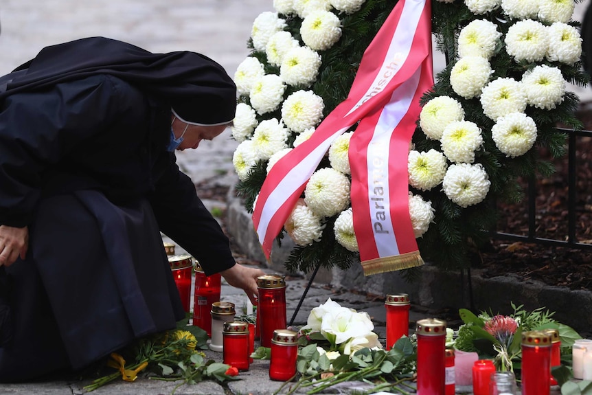 A nun places a candle in front of a wreath of leaves and white flowers.
