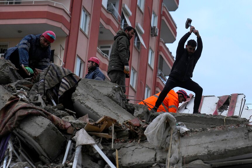 A man stands on top of a building with a tool to help break the debris. 