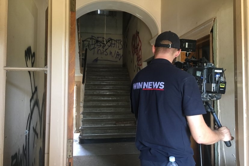 A cameraman filming inside a dilapidated house.