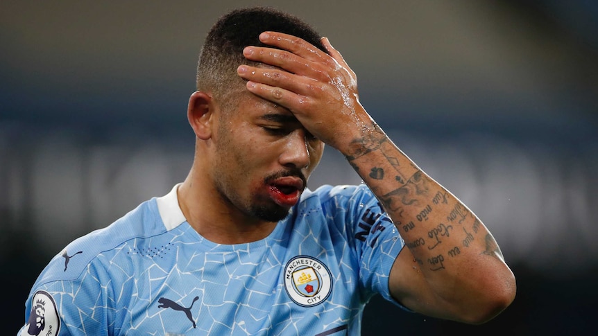 A Premier League footballer puts his hand to his head as he looks down at the pitch.