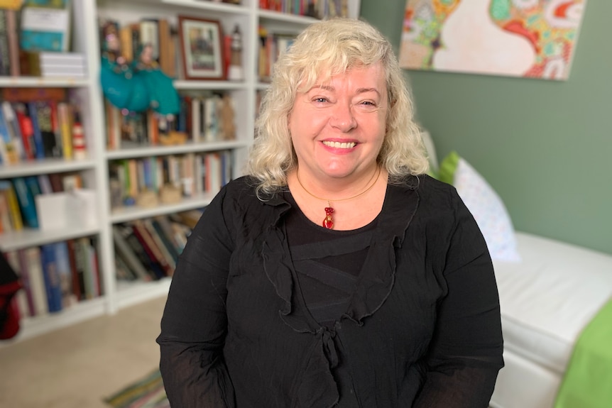 Hannah Dahlen sits and smiles at the camera, in front of a bookshelf full of books and photos.