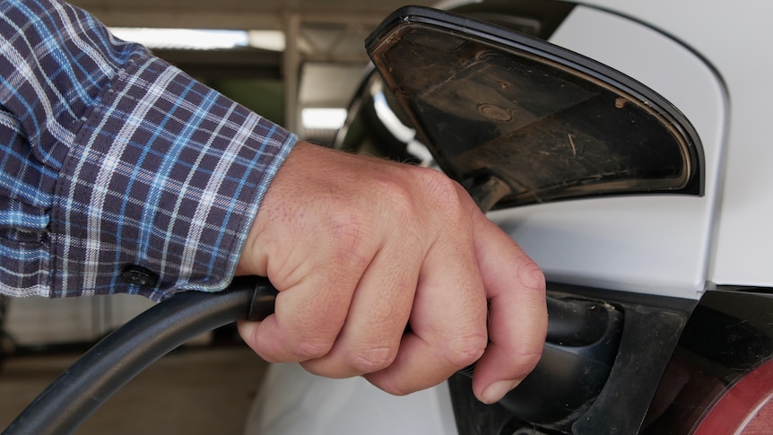 A man's hand holding a charging pump plugged into a white car