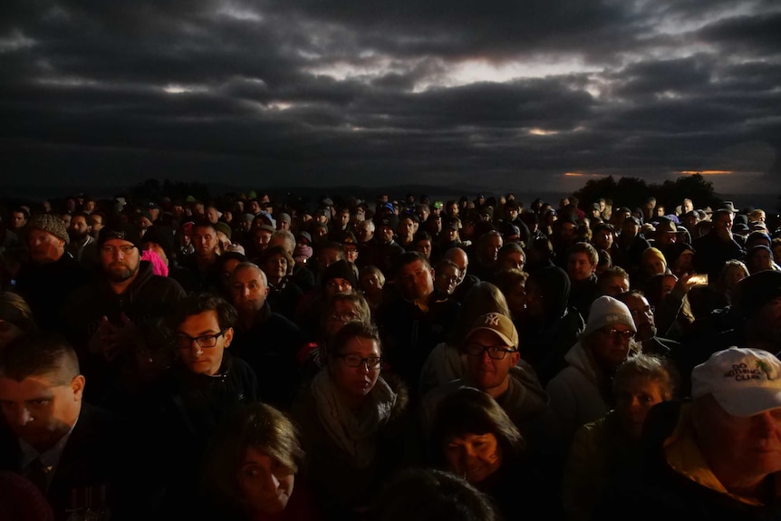 A wide shot of hundreds of people at dawn facing the camera for an Anzac service.