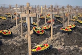 Red black and yellow wreaths sit on dirt graves under wooden crosses as far back as the horizon. 