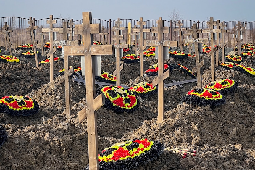 Red black and yellow wreaths sit on dirt graves under wooden crosses as far back as the horizon. 