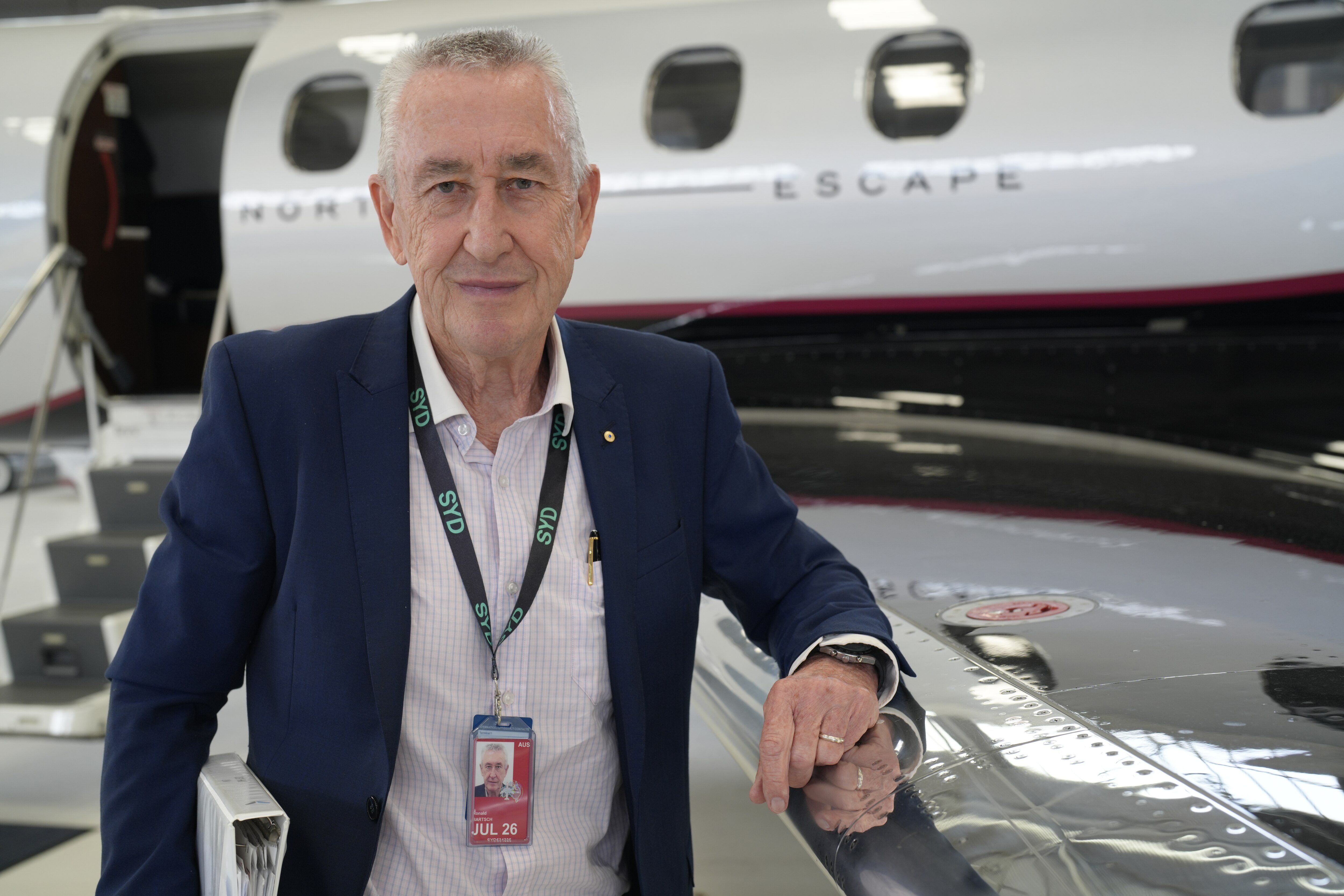 Older man in a navy suit jacket standing in front of a small plane.