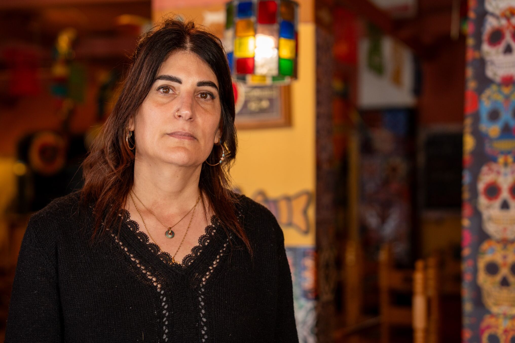 Uma mulher de cabelos castanhos fica com uma cara séria em frente a um restaurante colorido