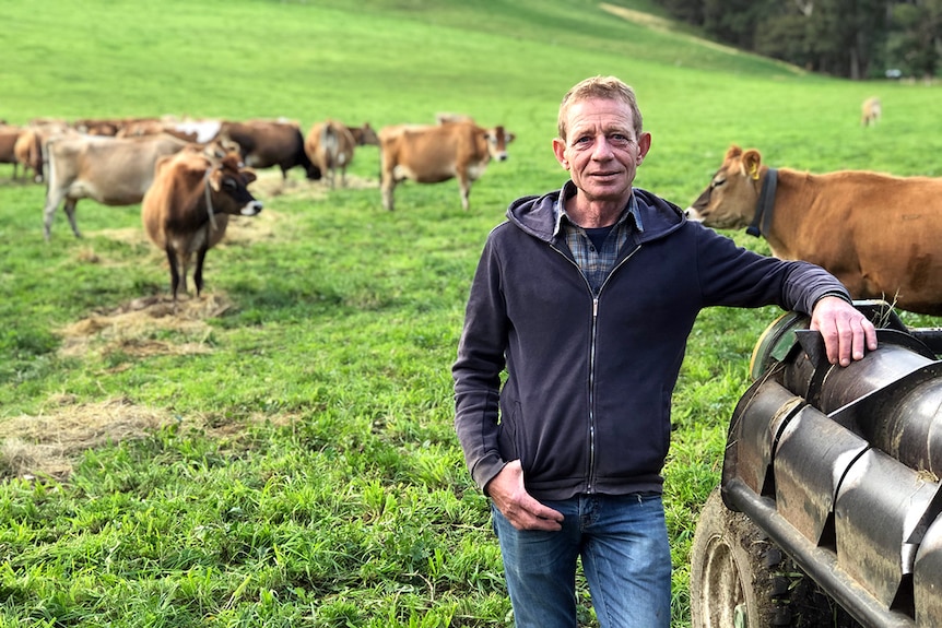Portrait of Paul Mumford leaning against a farm vehicle with Jersey dairy cattle and green grass in background.