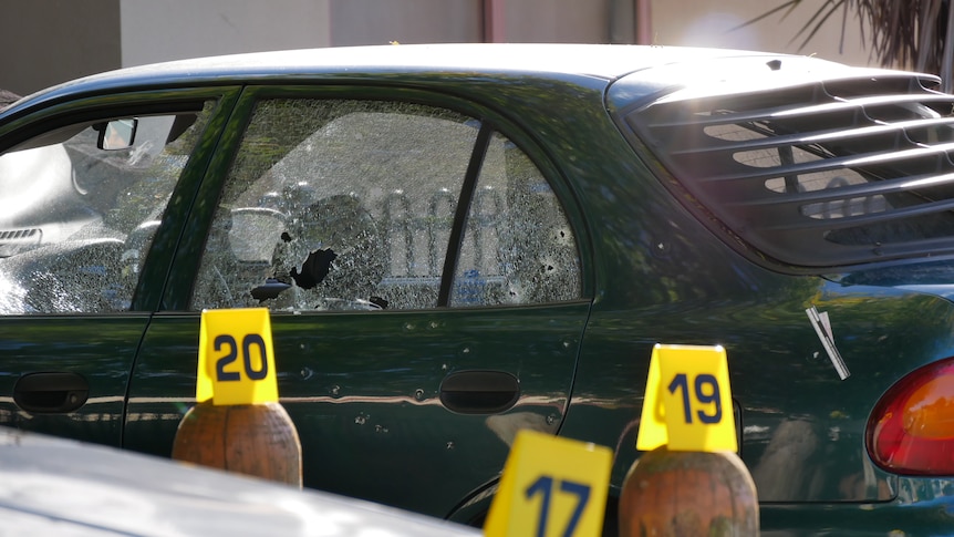 A green car with damaged windows and police incident identification numbers