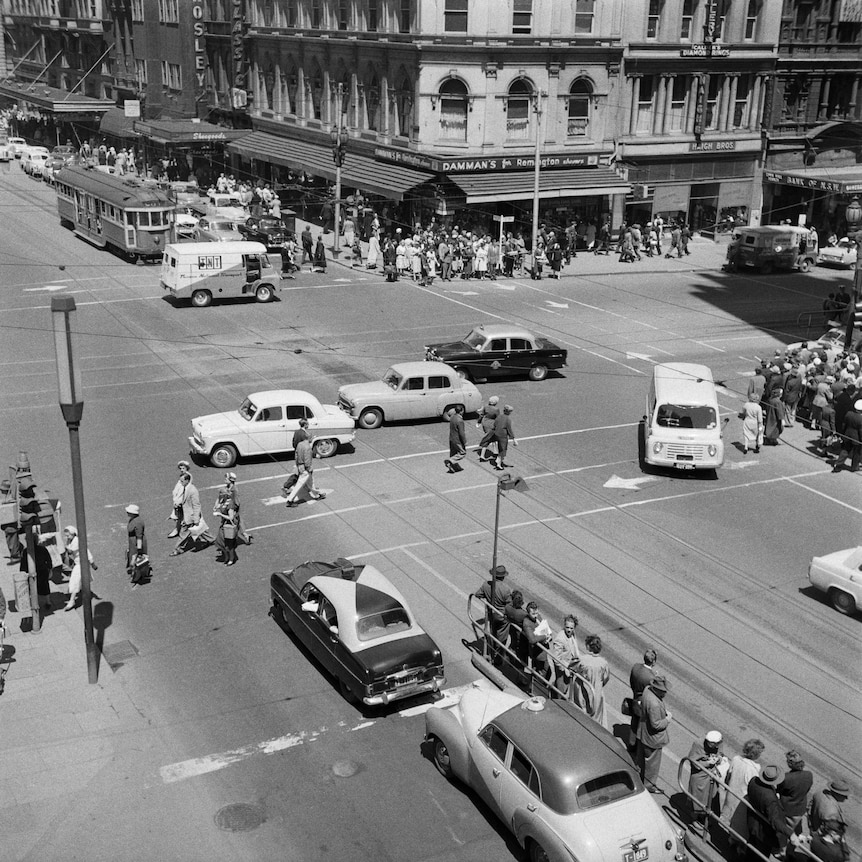 Cars, trams and pedestrians on a city street corner in the 1950s, shot from above