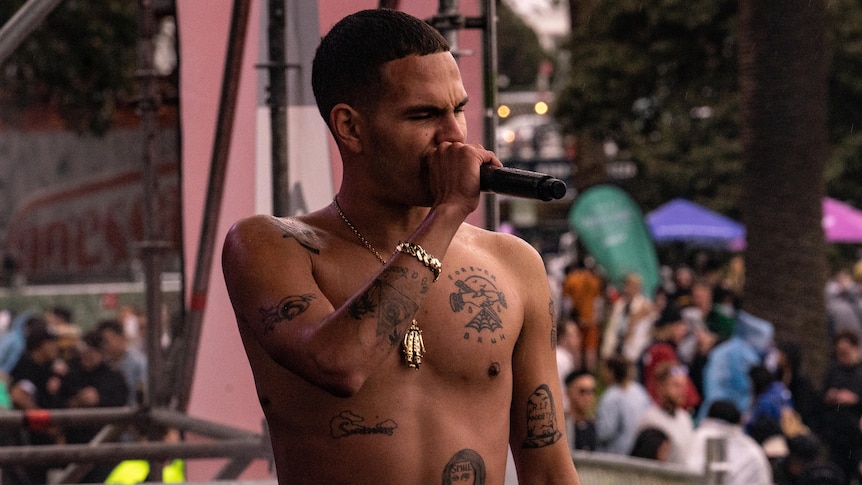Slowthai performs on an outdoor stage in Melbourne while shirtless, displaying his black ink tattoos.