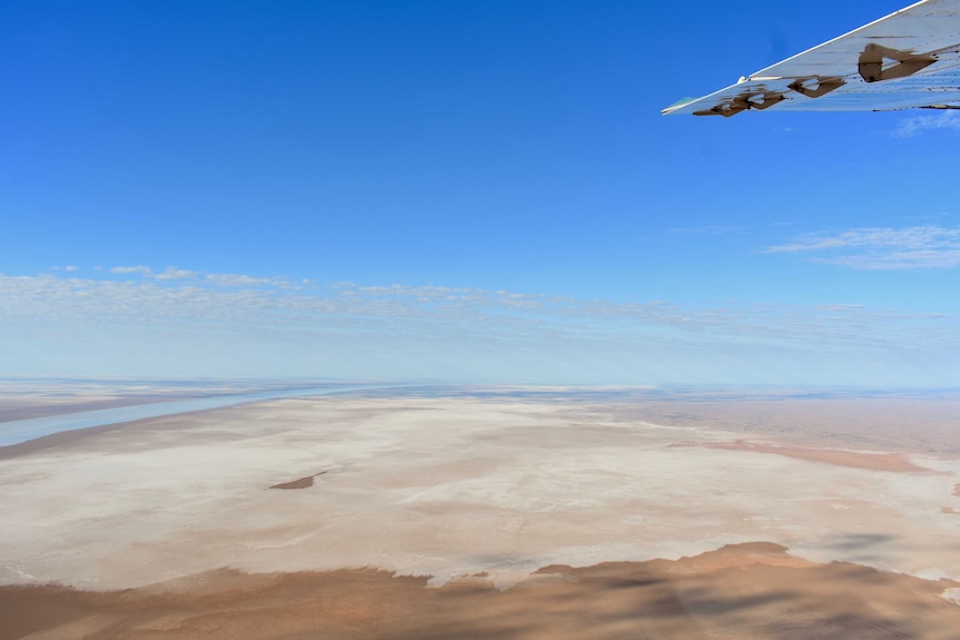 An aerial image of a large salt pan. There is water in the distance and a plane wing in the corner