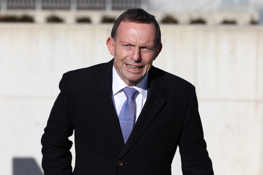 Tony Abbott arrives at Federal Parliament with bark blue suit, a white shirt, a like blue tie and a strained facial expression.